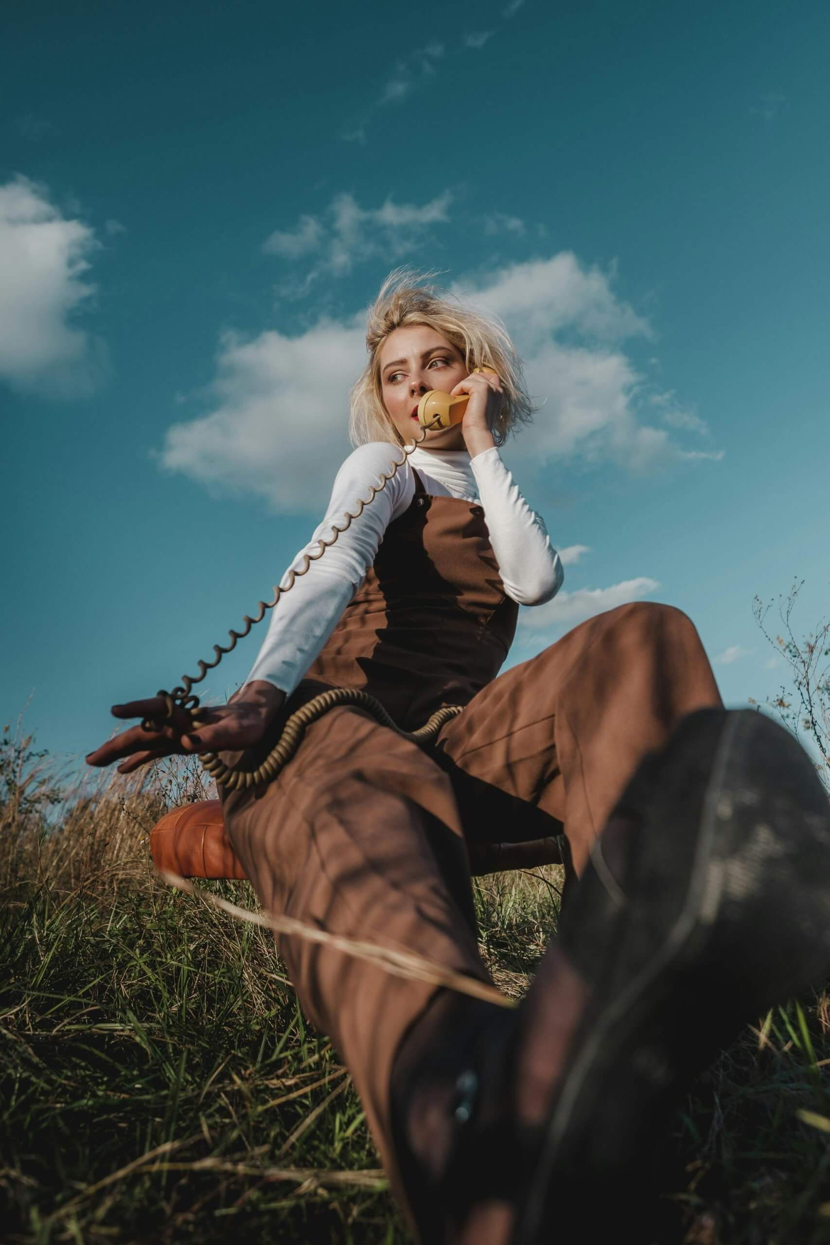 Low-angle shot of a woman in a field using a vintage telephone under a blue sky.